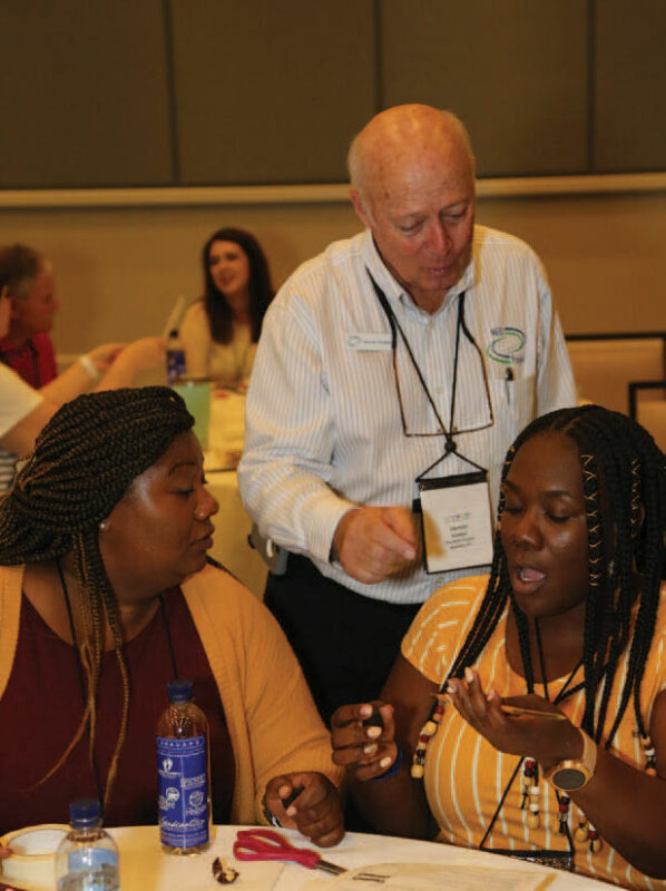 A man helping 2 workshop members with activites.
