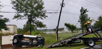 Car tipped over on side of road with a bent power pole nearby and emergency services there to help.